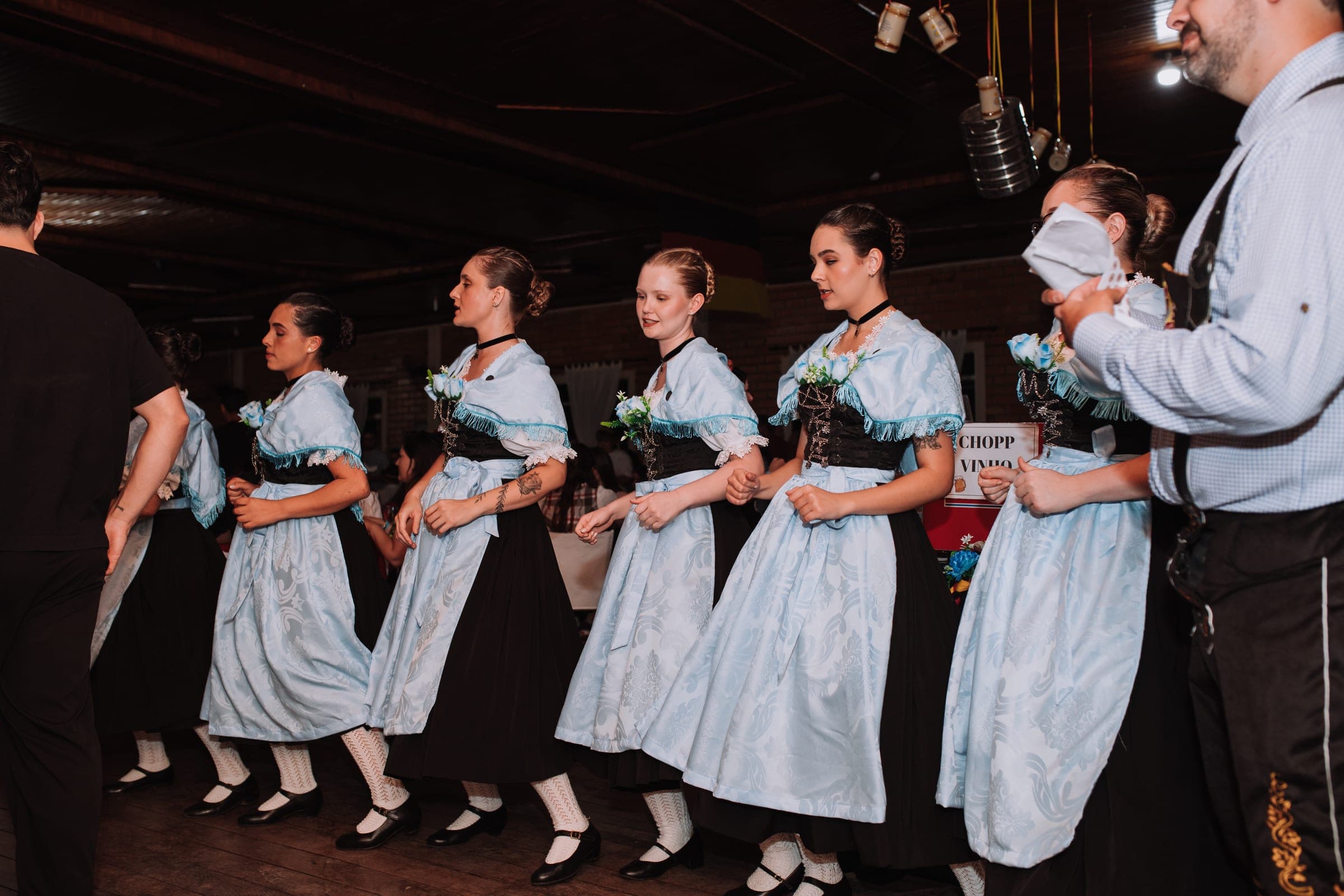 Dançarinas de vestido azul-claro dançando de braços dados durante a coreografia